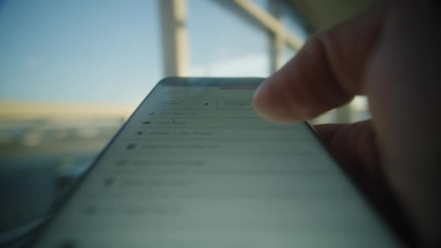 A traveler uses a smartphone to view a digital boarding pass and check flight details while waiting in a sunlit airport terminal