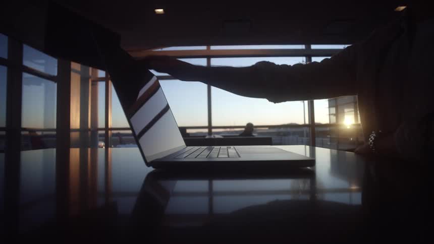A silhouetted person finishes working and closes their laptop in slow motion in an office with a view of the sunset