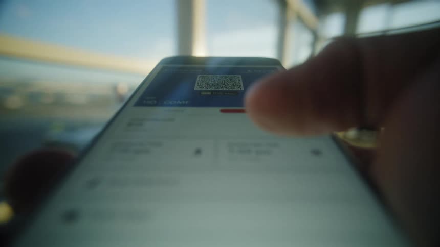 A traveler checks their flight details and mobile boarding pass on a smartphone at a sunlit airport gate