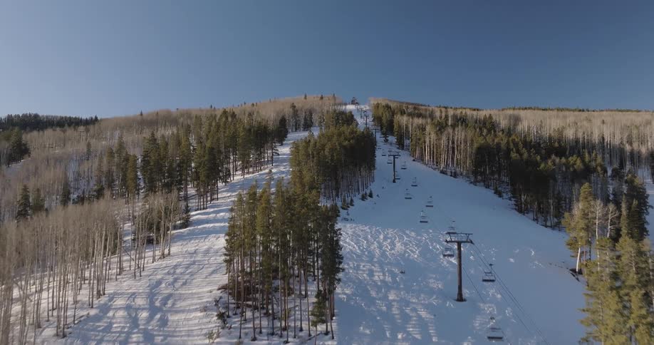 A serene aerial journey up a deserted ski mountain, following the path of an empty chairlift on a sunny winter day