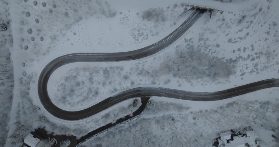 A slow top-down aerial zoom over a winding mountain road surrounded by a beautiful snow-covered winter landscape