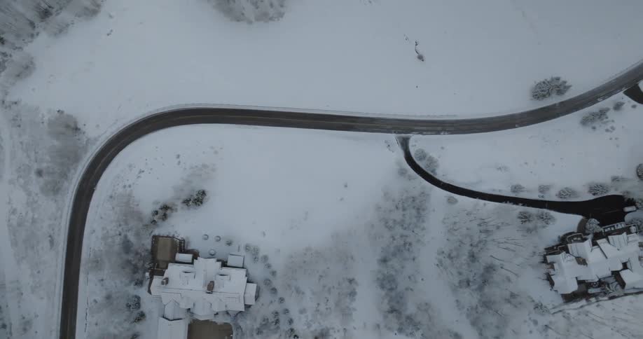 Aerial top-down shot reveals a luxurious mansion and winding road completely covered in a blanket of fresh winter snow