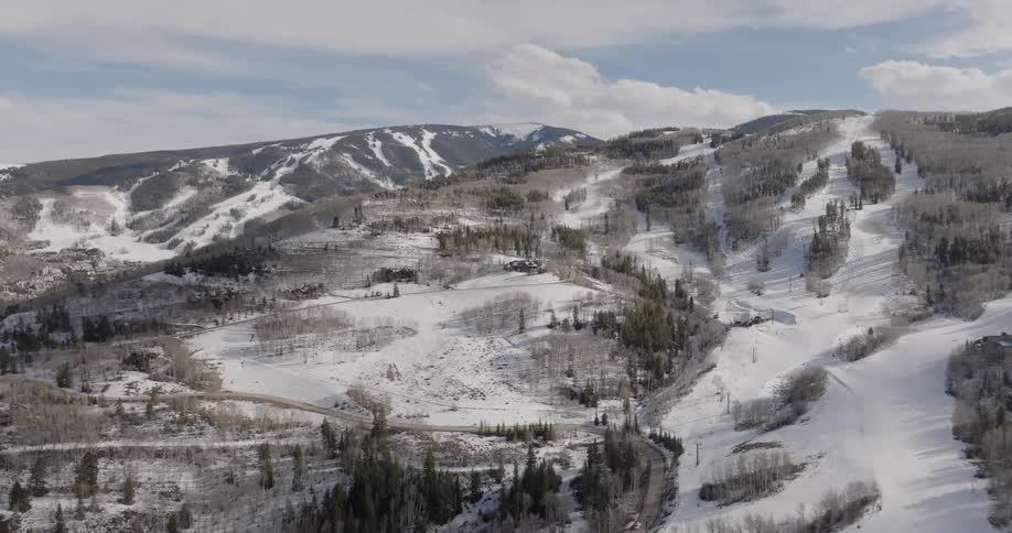 An expansive aerial shot slowly reveals a snowy mountain ski resort during the quiet spring off-season