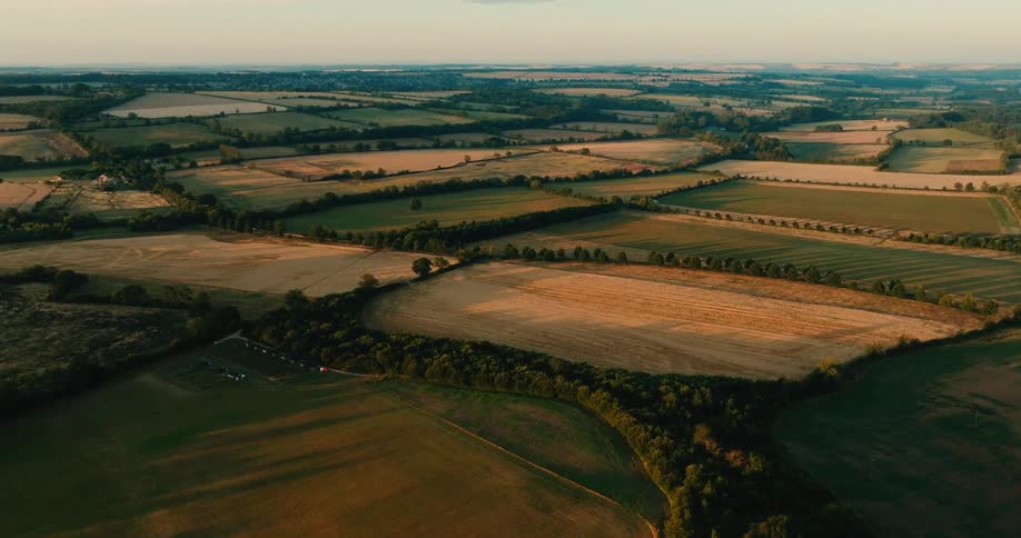 An expansive aerial view captures the patchwork of green and golden fields in the countryside during a serene sunset