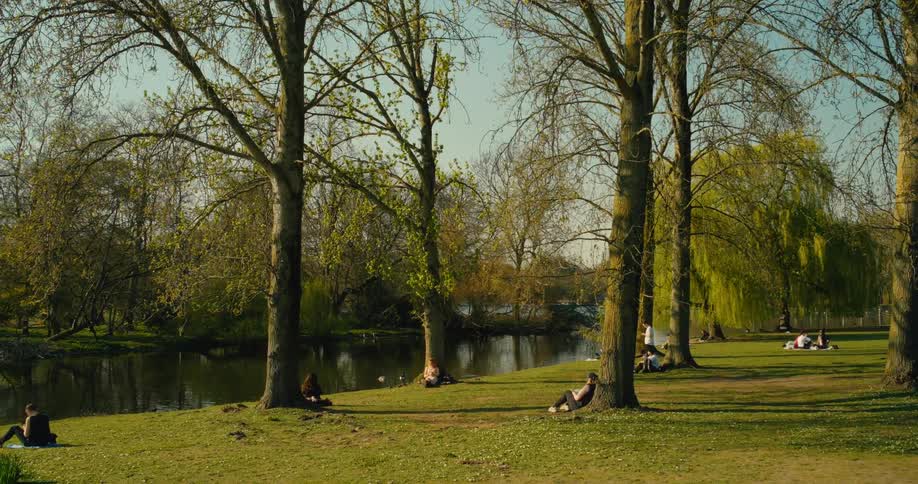 People enjoying a sunny spring day, relaxing on the grassy bank of a river in a tranquil park