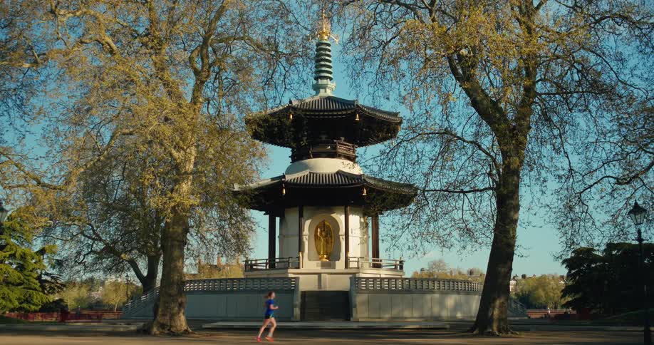 People jogging and cycling past the London Peace Pagoda in Battersea Park on a sunny day