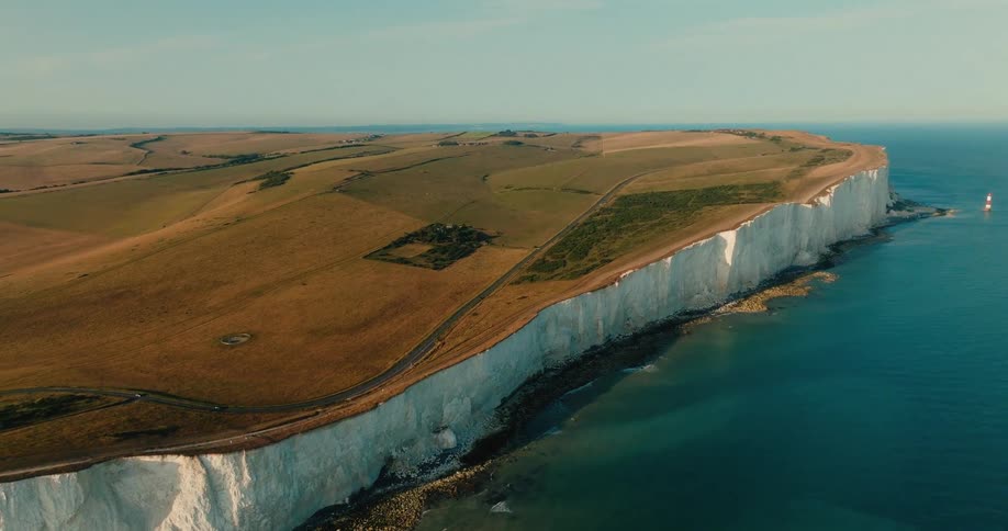 An expansive aerial shot captures the breathtaking beauty of the white chalk cliffs and rolling hills along the English coastline
