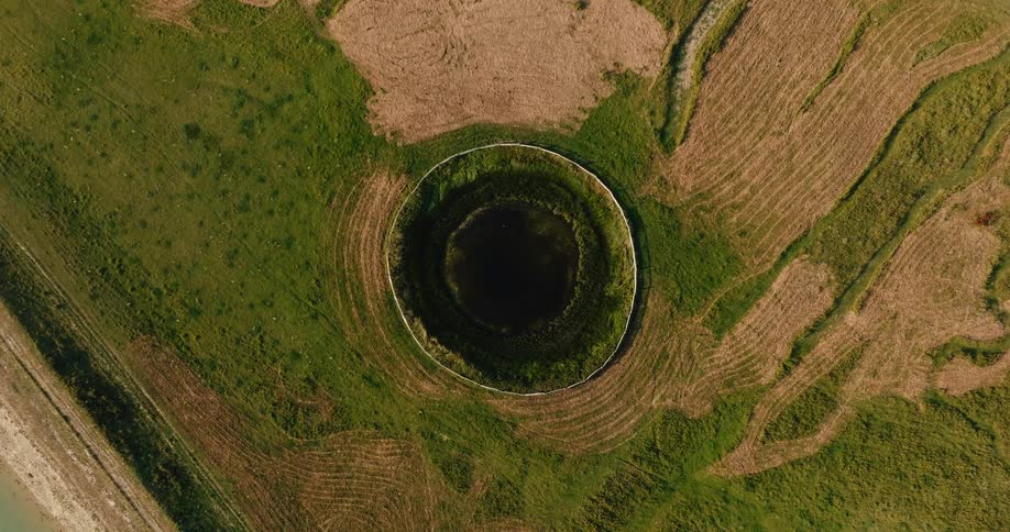 Hypnotic top-down drone shot slowly zooming into a perfectly circular dark pond in a rural landscape