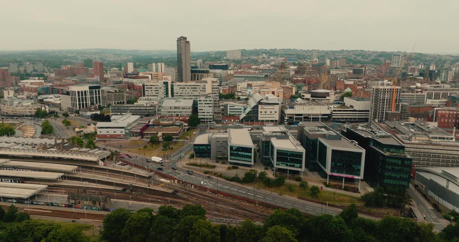 A slow aerial pullback reveals the Sheffield city skyline, with the bustling train station and city traffic below on an overcast day
