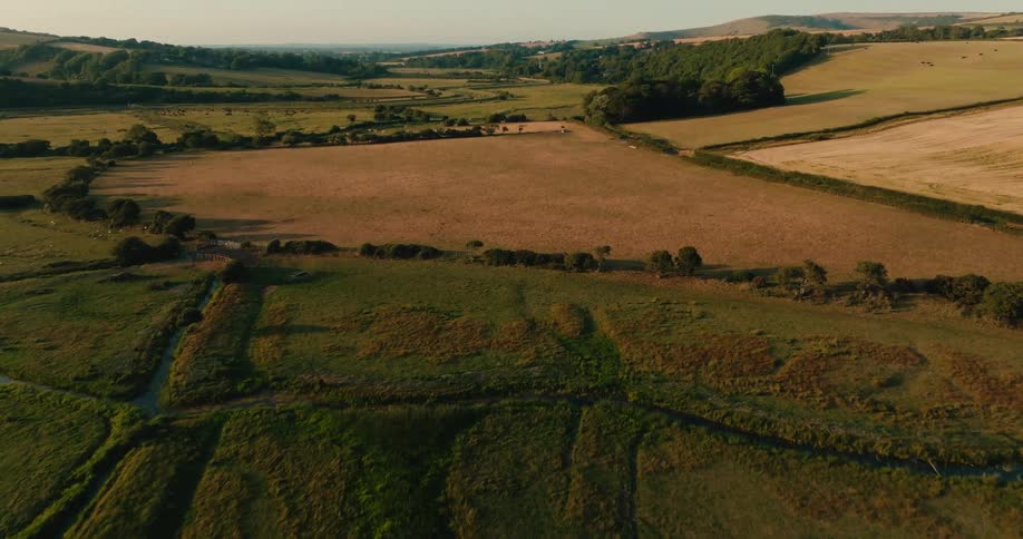 Slow aerial drone flight over a vast and picturesque rural valley with patchwork fields during a warm golden hour