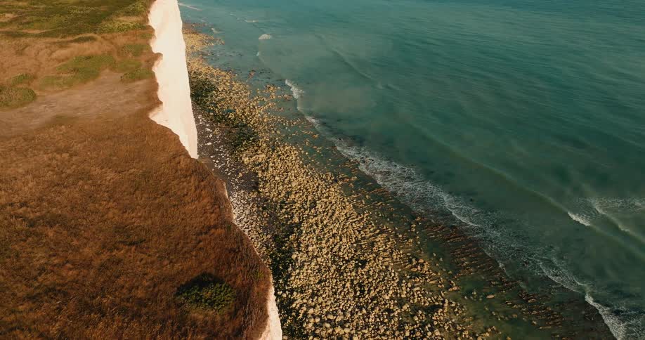 A stunning aerial view reveals the majestic white cliffs meeting the turquoise ocean along a rocky coastline during a beautiful sunset