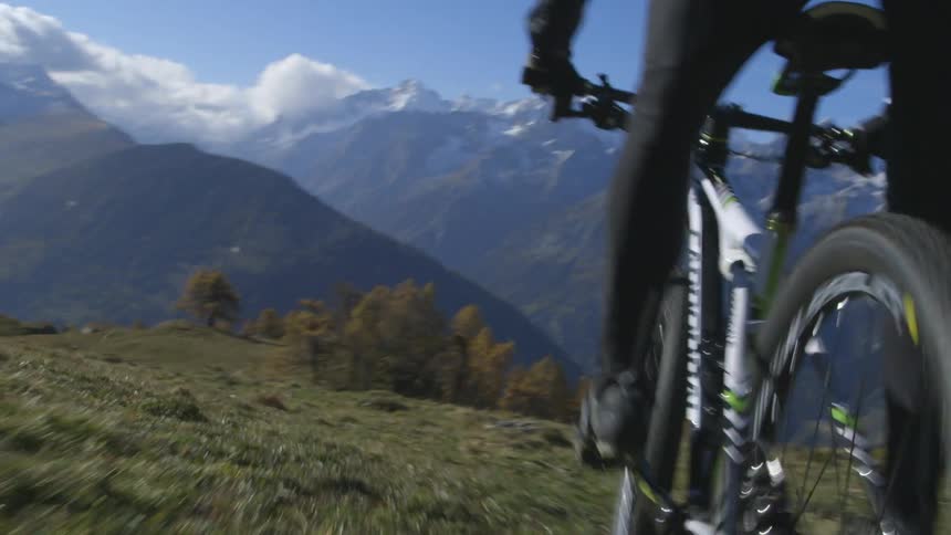 A rider rides a mountain bike in a hilly area with tall, snow covered mountains in the distance