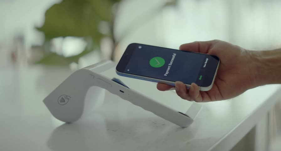 A close-up shot of a person making a successful contactless payment by tapping their smartphone on a modern POS terminal