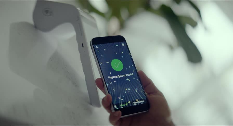 A person makes a contactless payment with a smartphone which displays a celebratory animation upon successful transaction