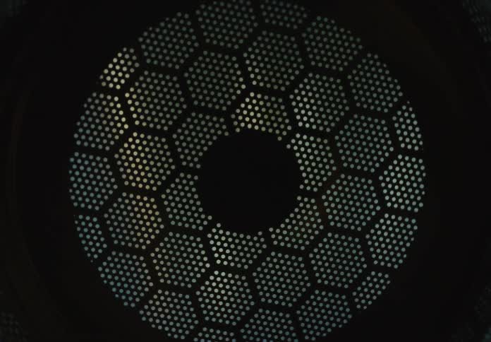 A mesmerizing light source rotates behind a dark, circular honeycomb metal mesh creating an abstract pattern