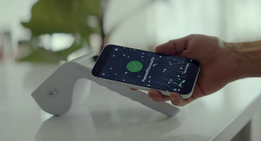 A dynamic, spinning close-up shot shows a successful contactless payment being made with a smartphone on a modern white POS terminal