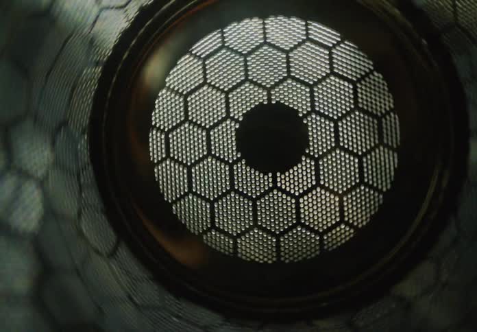 Flickering lights illuminate a metallic honeycomb mesh in a dynamic, abstract close-up