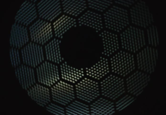 An abstract close-up of a shimmering light passing through a geometric honeycomb pattern in the dark