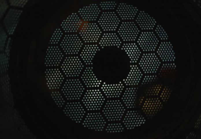 A strobing light flashes behind a circular honeycomb metal grid creating a pulsing effect