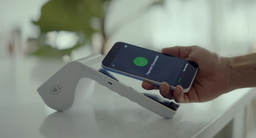 A person successfully completes a contactless payment using their smartphone on a modern point-of-sale terminal