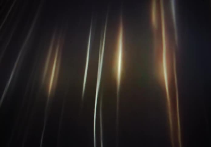 Flowing golden and white light streaks undulate gently against a dark, atmospheric background in this abstract animation