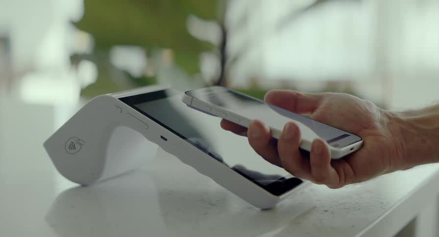Close-up of a customer making a secure, contactless payment by tapping their smartphone on a modern white POS terminal