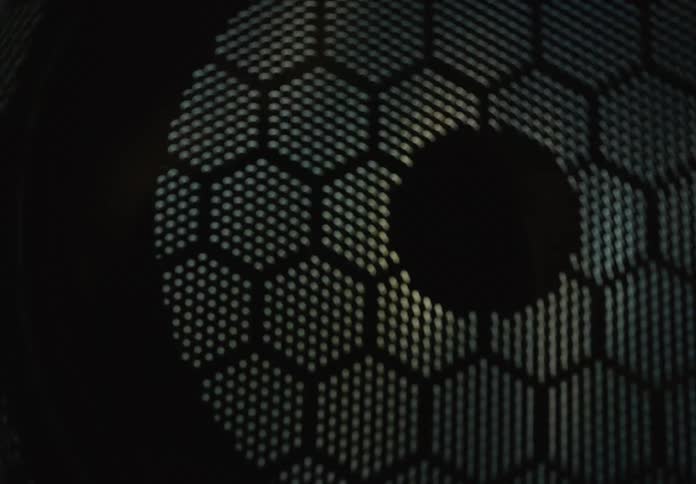 Shifting light creates a dynamic visual effect on a geometric perforated metal surface with a honeycomb pattern