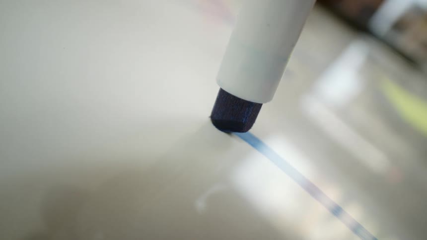 A macro close-up shot of a blue marker drawing a line on a glossy white board