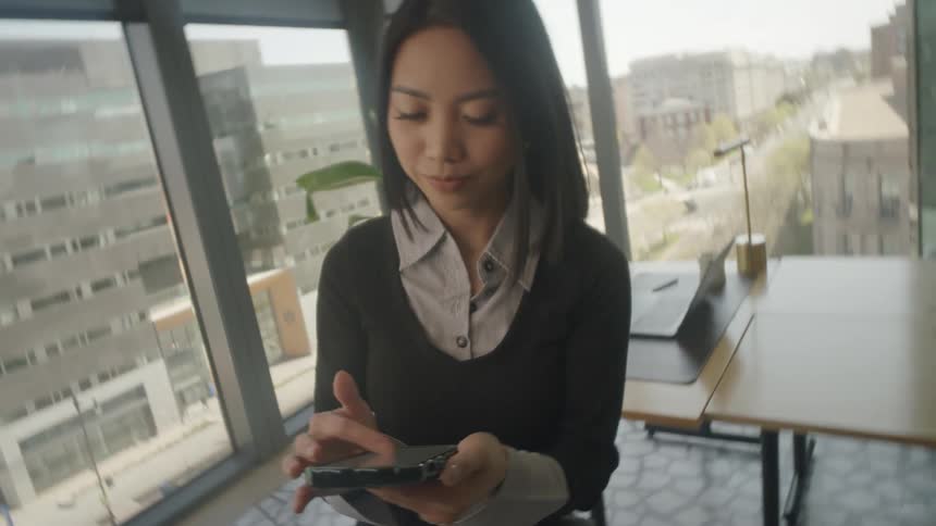 A dynamic spinning shot reveals a businesswoman scrolling on her smartphone in a modern city office