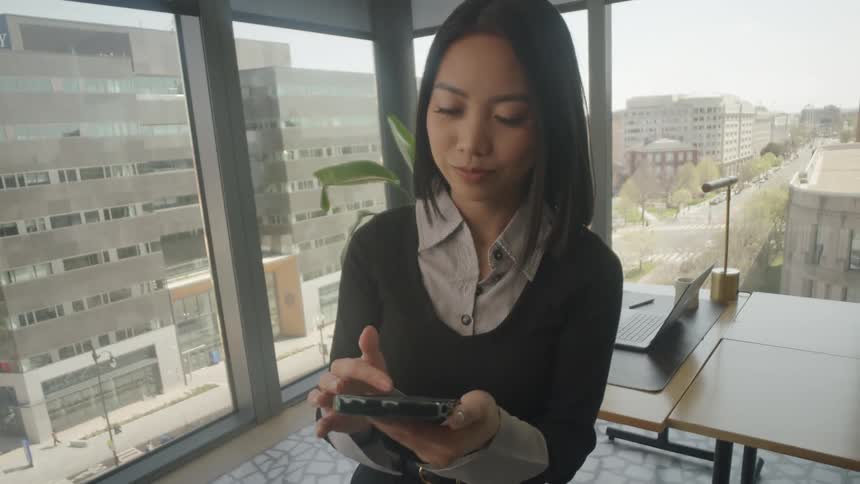A dizzying camera move pulls back from a close-up of a businesswoman scrolling on her phone to a wide shot revealing her in a bright city office