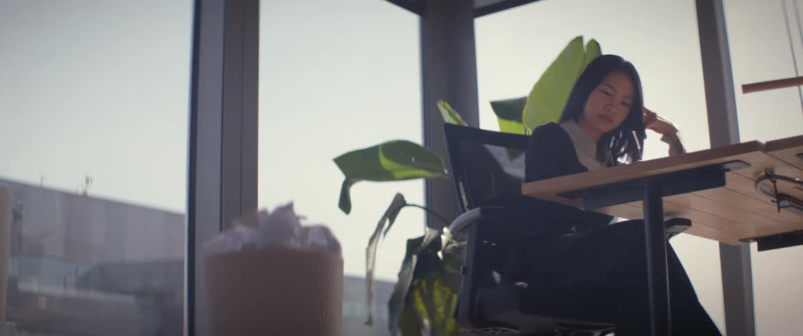 A frustrated woman with writer's block crumples paper and tosses it into a full wastebasket in a sunlit office in slow motion