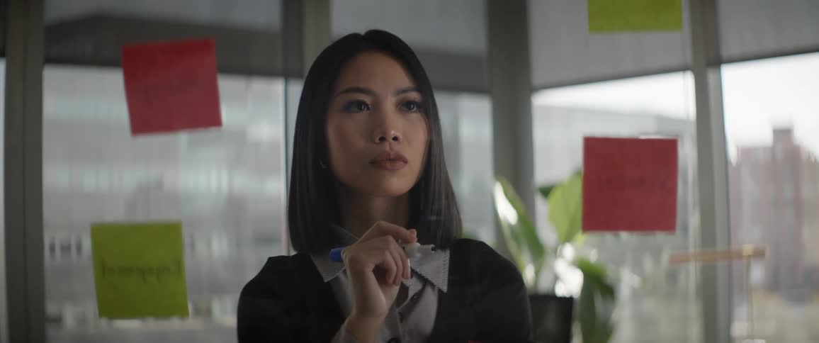 A creative Asian businesswoman stands thoughtfully, holding a marker, while looking at a planning board with colorful notes