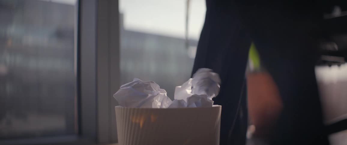 A crumpled piece of paper is tossed into a trash bin in slow motion, symbolizing writer's block or discarded ideas