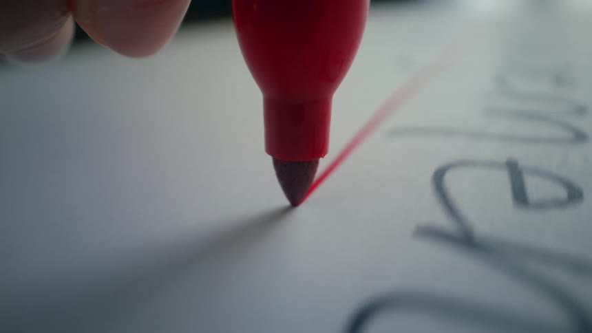 Macro view of a red marker crossing out handwritten black text on a white sheet of paper