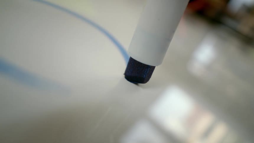 A macro close-up of a blue marker drawing a curved line on a glossy whiteboard surface