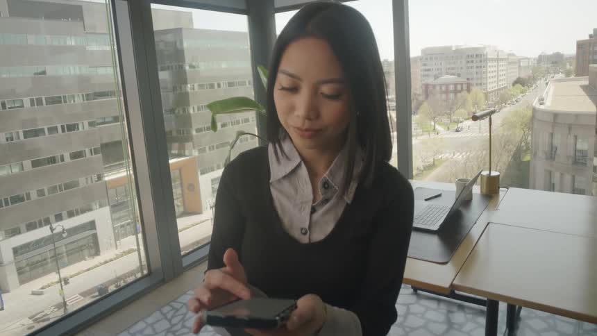 Fast-spinning camera effect settles on a young professional woman using her mobile device in a modern city office