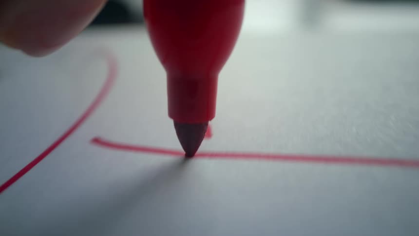 An extreme close-up view of a red marker tip as it draws abstract lines on a white surface