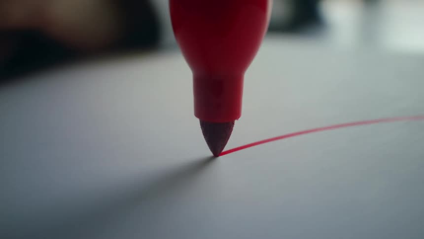 Close-up macro view of a red felt-tip marker drawing a straight line and a circle on white paper