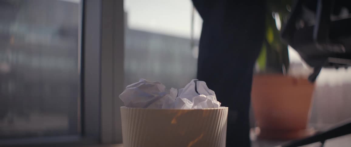 A crumpled paper ball is tossed into a small wastebasket on a desk in an office