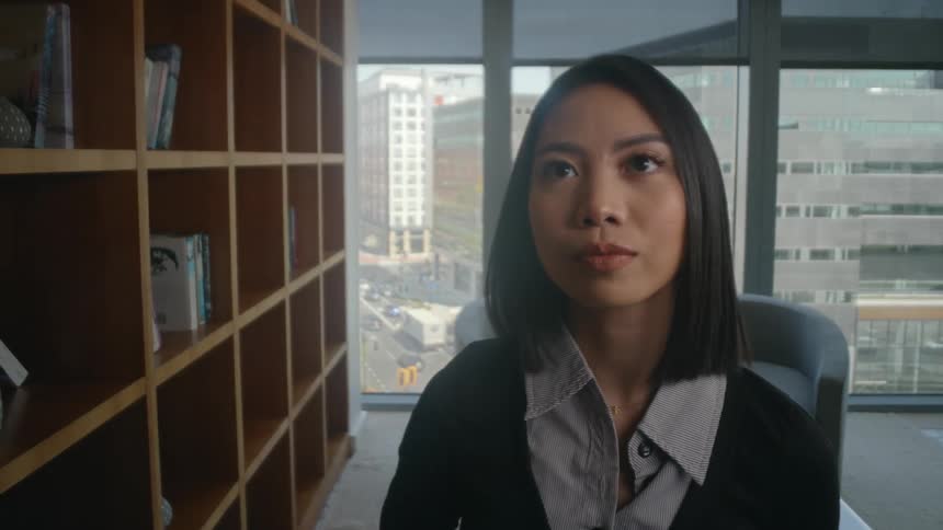 POV shot from inside a bookshelf as a professional woman in a city office places a large book on the shelf, covering the camera
