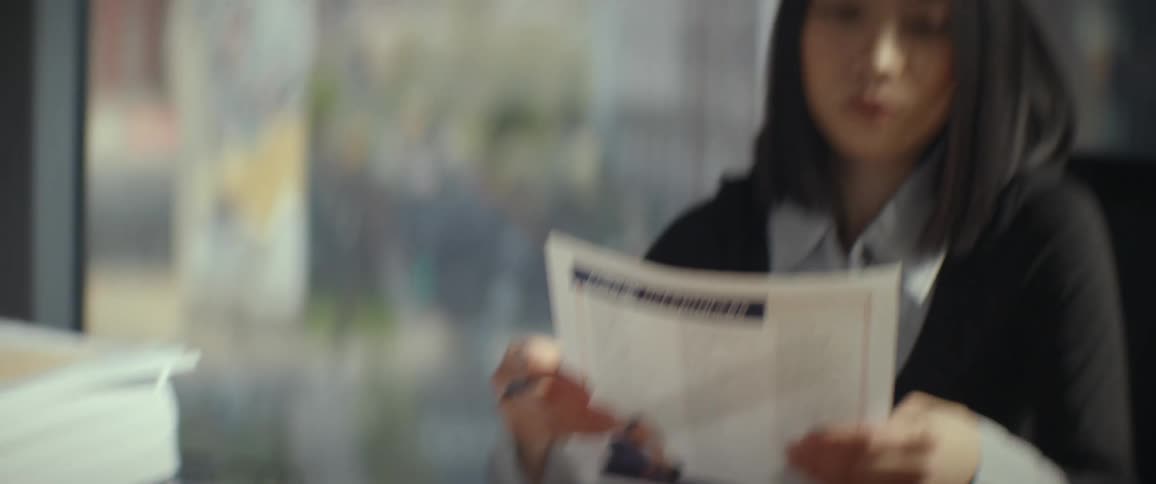 A focused businesswoman diligently reviews and signs documents from a large stack at her modern office desk