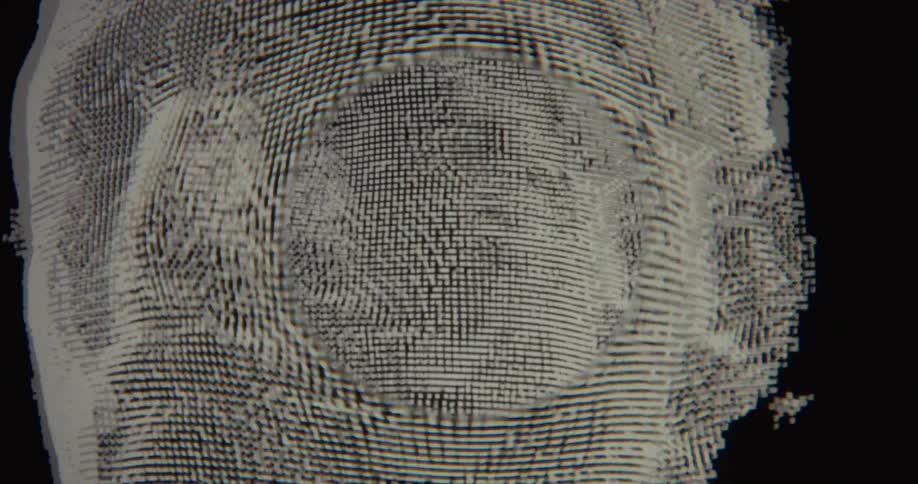 A close-up shot shows a 3D digital model of a human head, made of shifting pixels, being manipulated and rotated on a computer screen