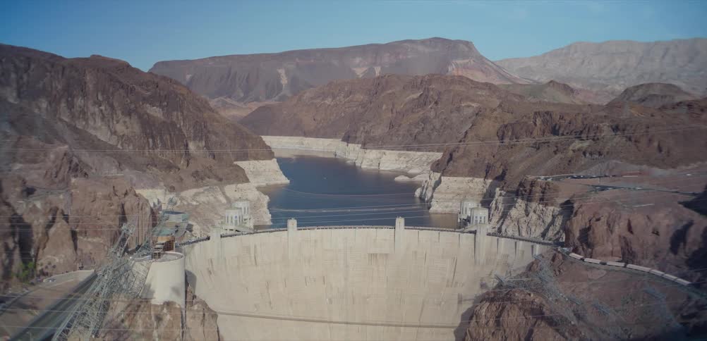 A wide, scenic daytime view of the massive Hoover Dam and Lake Mead nestled within a dramatic desert canyon