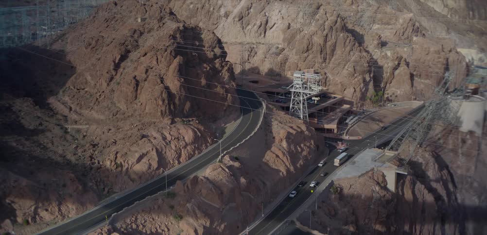 A high-angle view of traffic moving along a winding highway through the rocky, arid mountains near the Hoover Dam