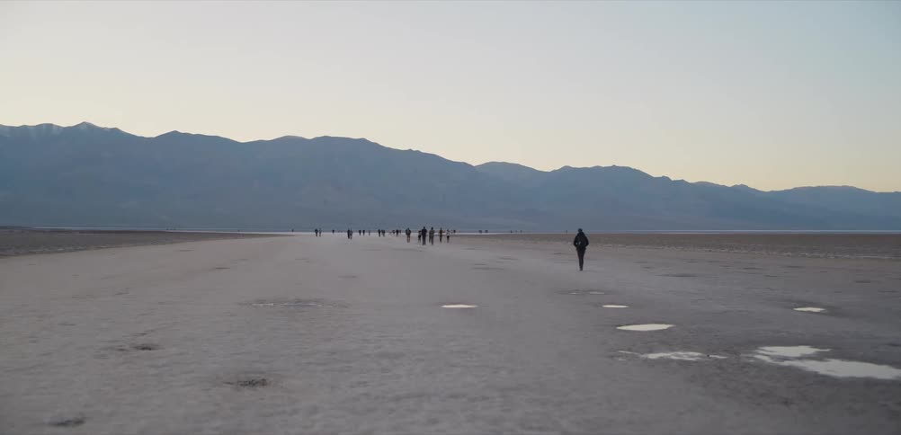 Tourists walk across the vast salt flats of Badwater Basin in Death Valley National Park during a cool, hazy sunset