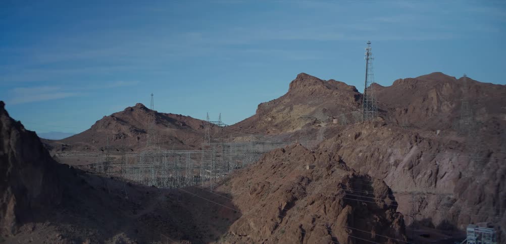 An electrical substation and power lines are nestled in a rugged, rocky canyon landscape