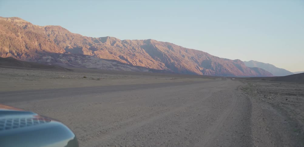 A static shot from inside a vehicle captures a vast, arid desert landscape and distant sunlit mountains at golden hour