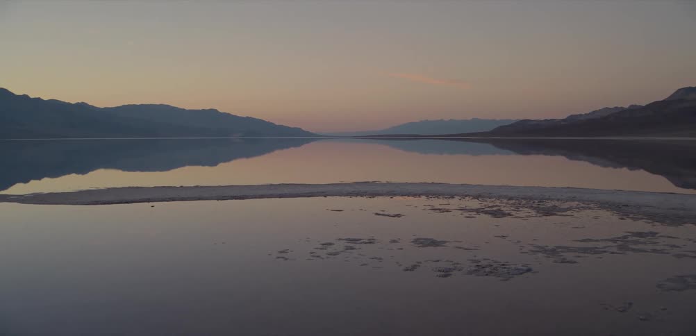 A serene lake perfectly reflects the surrounding mountains and colorful sky at dusk
