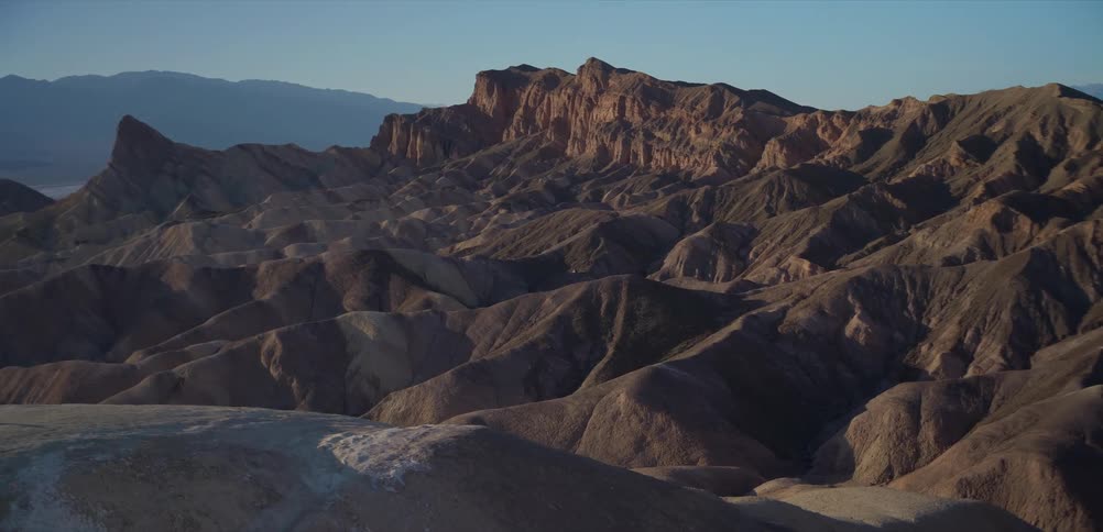 The first light of day slowly creeps across the desolate, rolling hills and mountains of a desert landscape