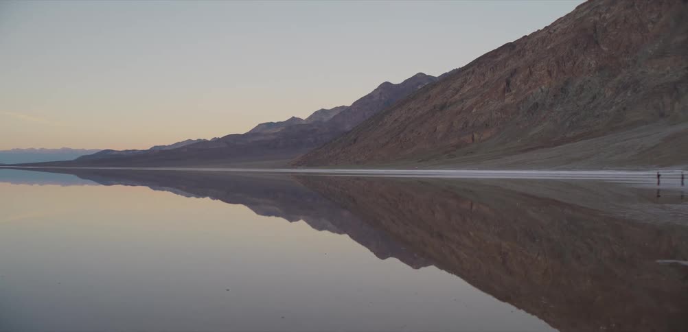 A serene desert mountain range creates a perfect mirror-like reflection in the still water at dawn